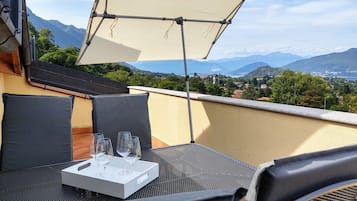 Un balcone con un tavolo apparecchiato per due persone, un vassoio bianco con dei bicchieri e un tendaggio che fa ombra.
