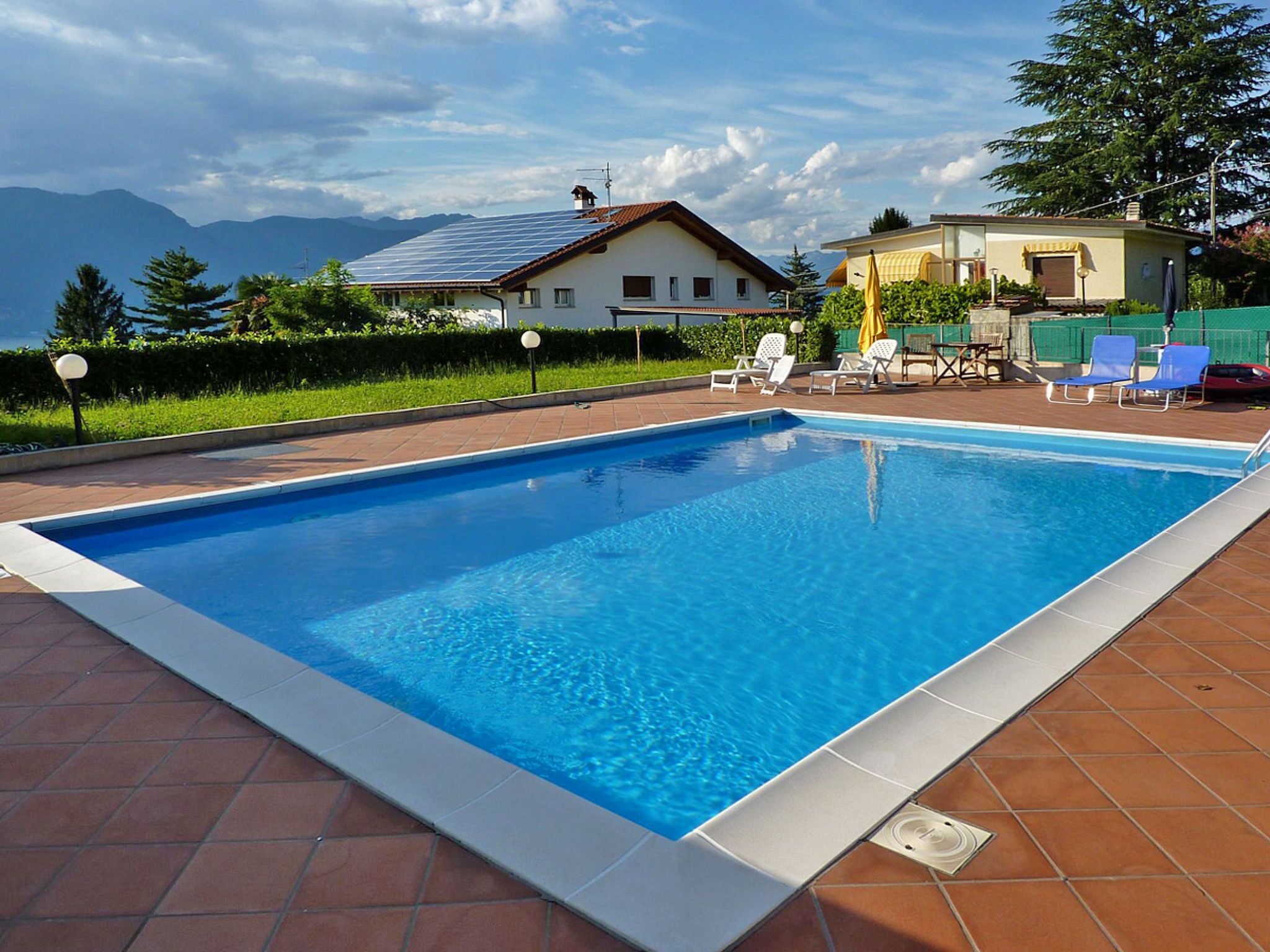 Ein rechteckiger Pool mit einer gefliesten Kante, umgeben von einer Terrasse mit Stühlen und einem Tisch.