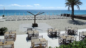 Un restaurante frente a la playa con terraza, una palmera y vistas al océano.