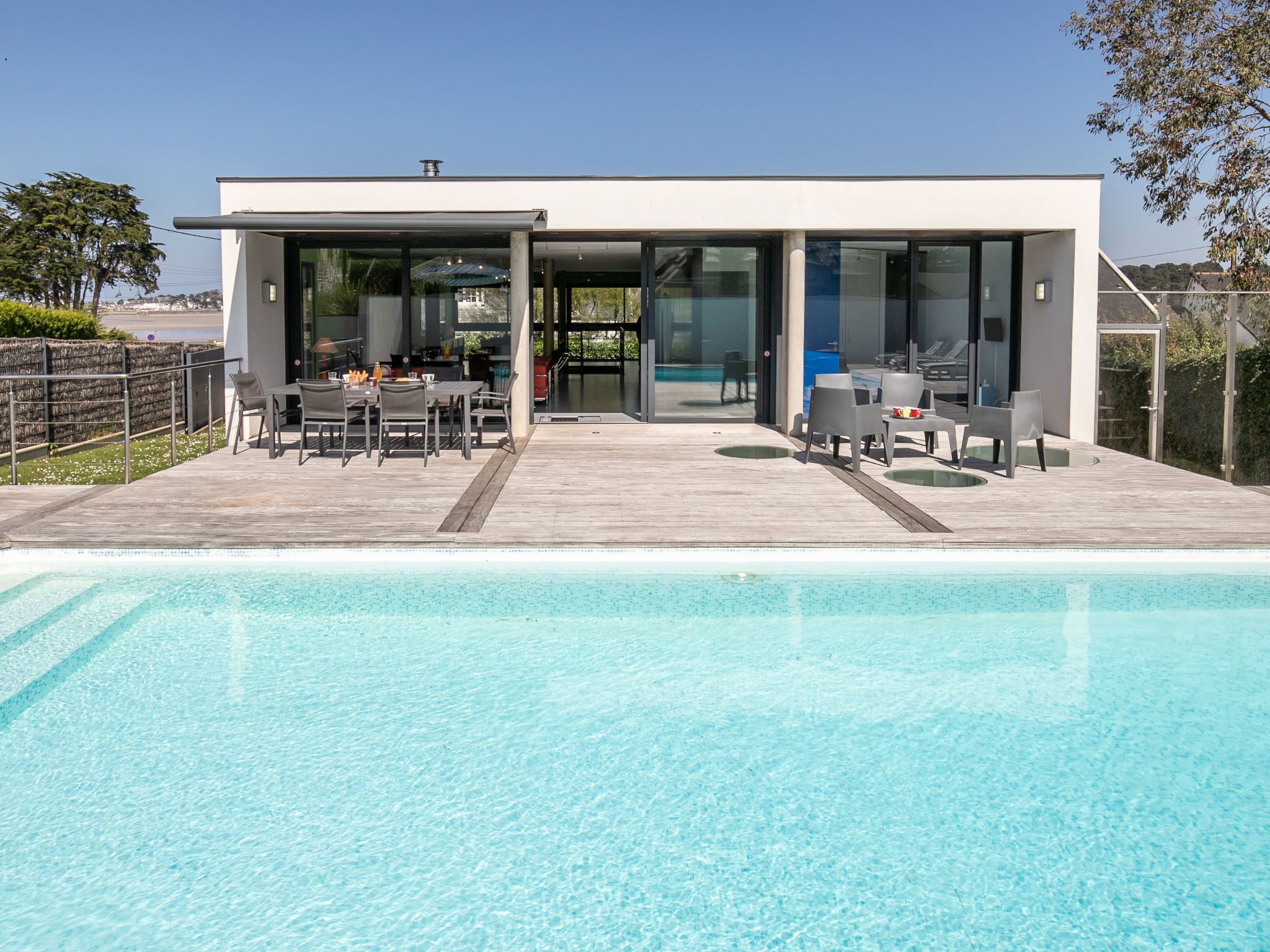 A modern house with a swimming pool, a patio with outdoor furniture, and a glass door leading to the pool area.