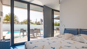 A modern bedroom with a large bed, a view of a pool and outdoor seating, and a sliding glass door leading to an outdoor area. - Villa de la Baie by Interhome (Locquirec)