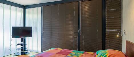 Un dormitorio con una colcha colorida, un televisor sobre un mueble bajo y un armario con puerta corrediza.
