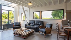 Un vaste espace de vie agrémenté d’un canapé en cuir noir, d’une table basse en bois et de fauteuils en osier. De grandes fenêtres offrent une vue sur la verdure environnante.