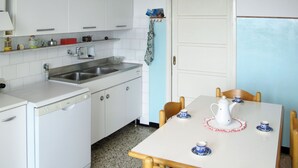 A compact kitchen with a sink, stove, and a dining area with a table and chairs. - Casa del Pernambuco (PTL205) by Interhome (Pietra Ligure)