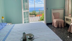 A room with a bed, a chair, a table, and a view of the sea through an open door. - Casa del Pernambuco (PTL205) by Interhome (Pietra Ligure)