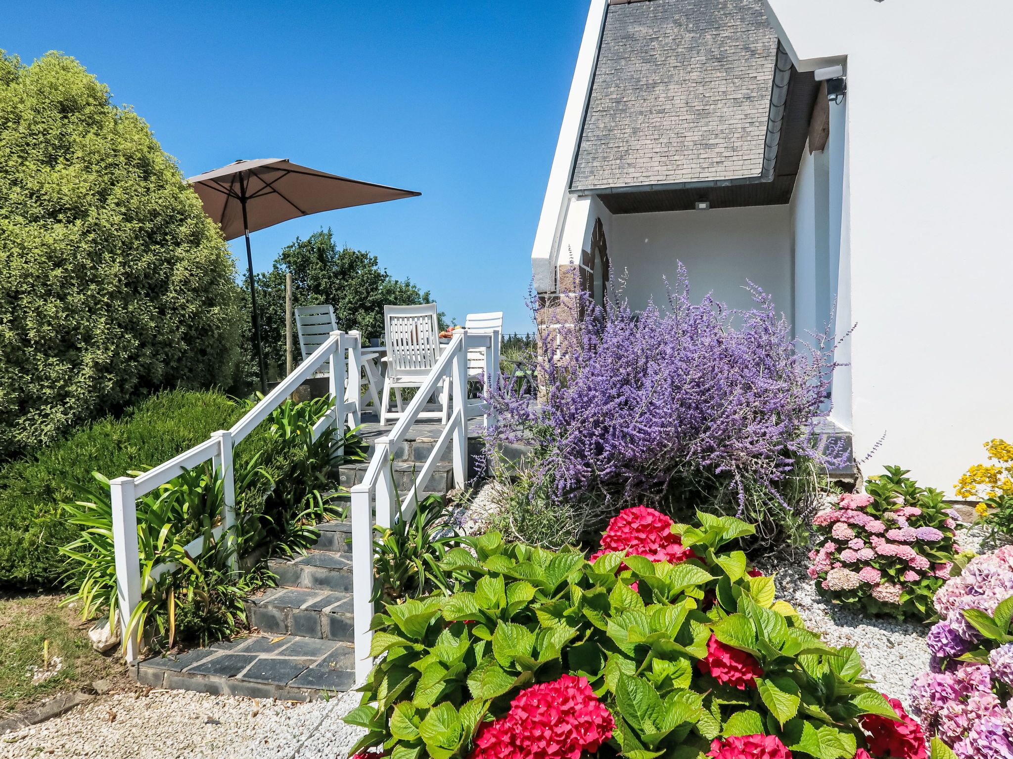 A staircase leading to a building with a white exterior, surrounded by lush greenery and vibrant flowers.