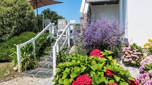 Eine Treppe führt zu einem Gebäude mit weißer Fassade, umgeben von üppigem Grün und bunten Blumen.