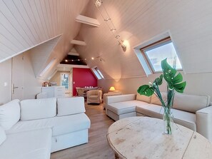 A modern loft-style room with a high ceiling, white furniture, a dining area, and a large window.