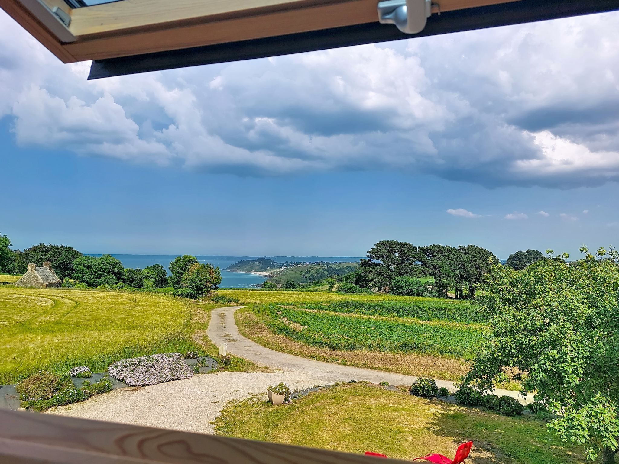 A scenic view from a window overlooking a rural landscape with a dirt path, greenery, and a distant body of water.