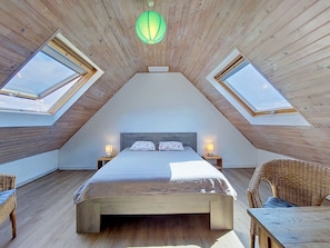 A bedroom with a sloped ceiling, skylights, a bed, bedside lamps, and a wicker chair. - La Belle Vue by Interhome (Locquirec)