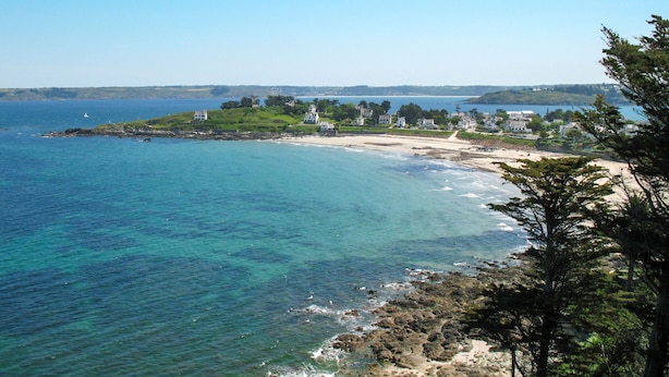Uma área costeira com uma praia, um pequeno conjunto de edifícios brancos e uma vista clara do mar.