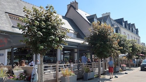 Um restaurante com mesas ao ar livre, um letreiro que diz "Place du Port" e um céu claro.