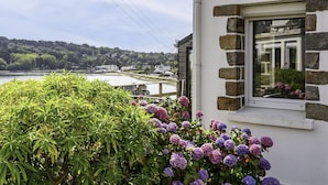 A house with a stone facade, a window with a view of a river and hills, and lush greenery in the foreground. - Ti an Aod by Interhome (Plougasnou)