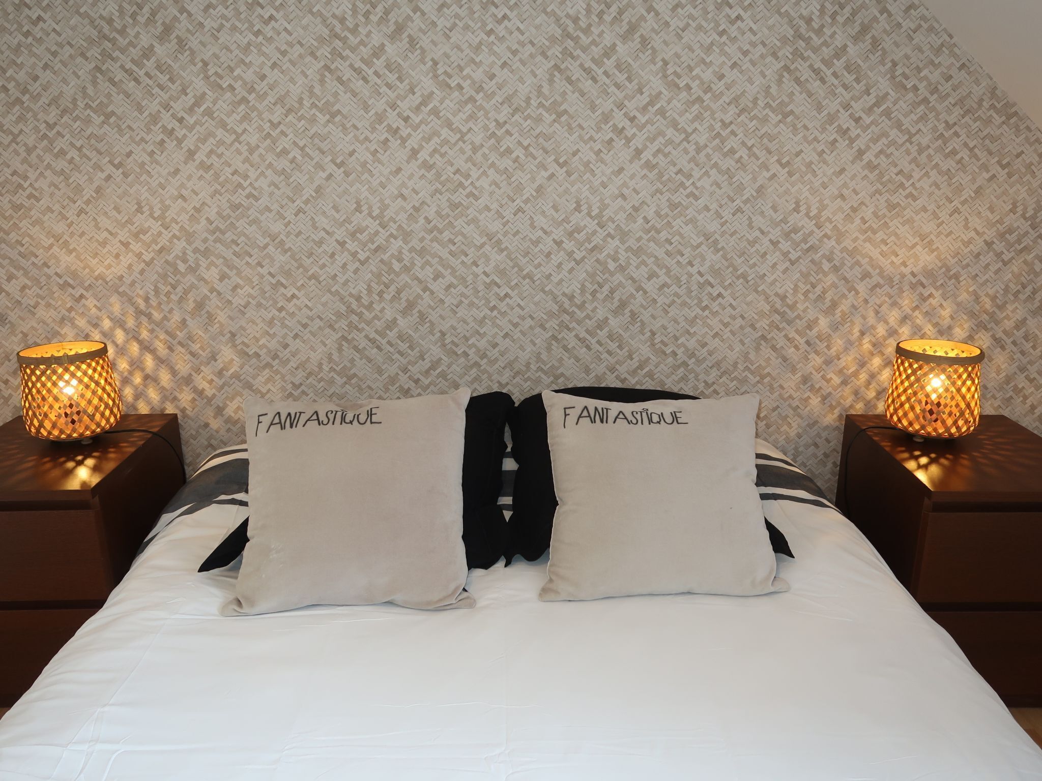 A bed with two pillows labeled "FANTASTIQUE," a patterned wallpaper, and two bedside lamps.