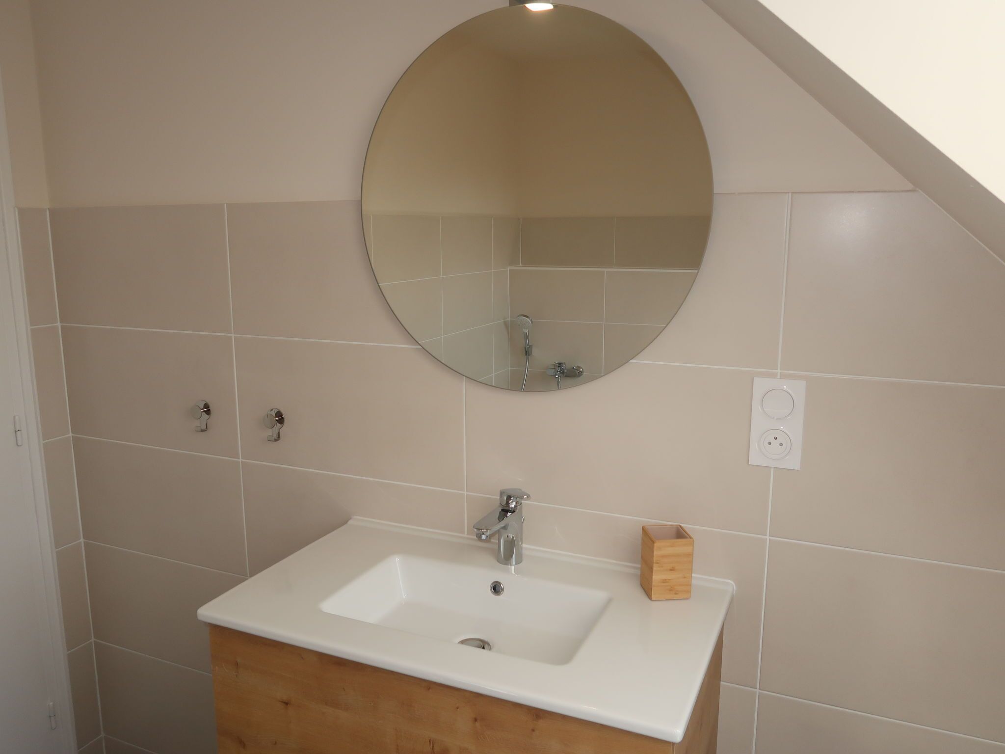 A bathroom with a white sink, a round mirror, and a wooden cabinet.