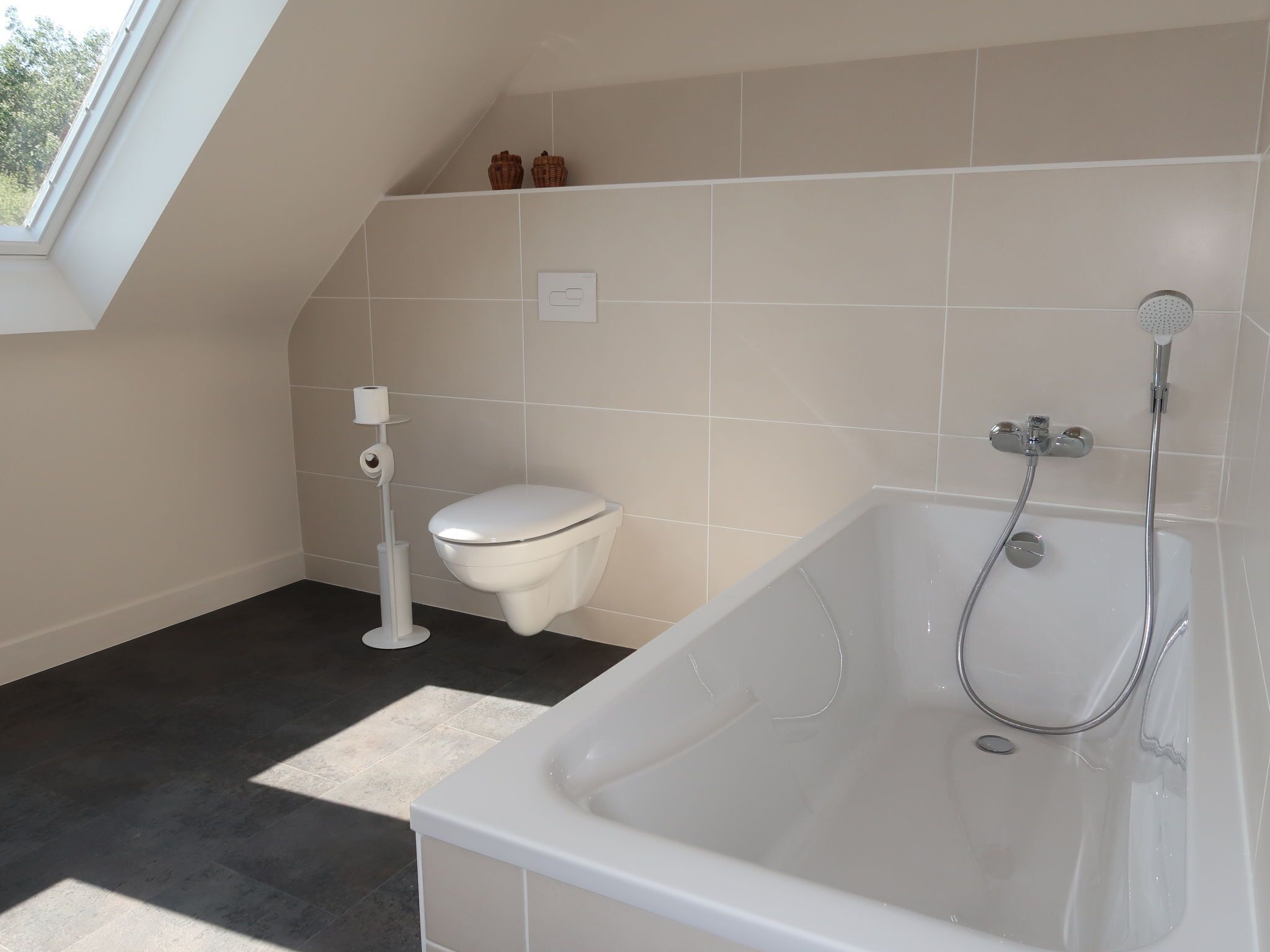 A modern bathroom with a white toilet, a bathtub with a showerhead, and a skylight above.