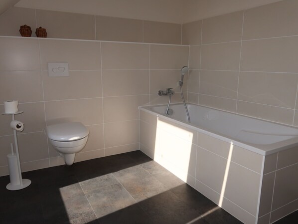 A bathroom with a toilet, a bathtub, and a toilet paper holder.