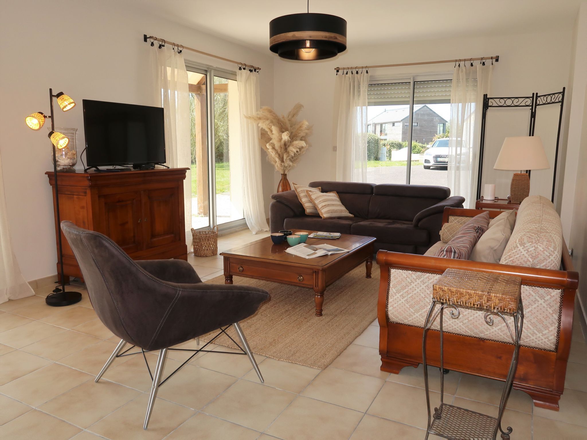 Een woonkamer met een bank, fauteuil, salontafel, televisie en decoratieve planten.