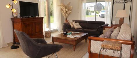 Een woonkamer met een bank, fauteuil, salontafel, televisie en decoratieve planten.