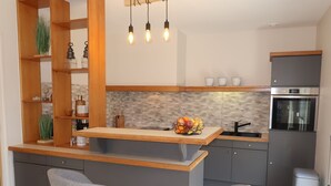 Een moderne keuken met een houten keukeneiland, twee grijze barkrukken, een inbouwoven en een roestvrijstalen koelkast.