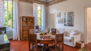 A dining area with a round wooden table, chairs, a cabinet with glassware, a white sofa, and a radiator. - Costanza & Valeria (PRE133) by Interhome (Molini di Prelà)