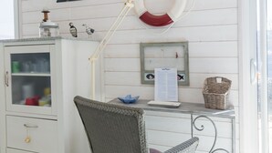 A room with a white cabinet, wicker chair, a desk with a lamp, a life preserver decoration, and a lighthouse model. - Penn an Aod by Interhome (Kerlouan)