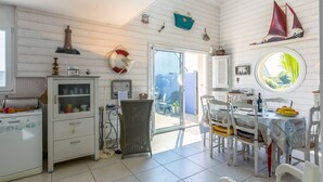 A spacious kitchen with white cabinetry, a dining area with a round table, and a view through a glass door to the outside. - Penn an Aod by Interhome (Kerlouan)