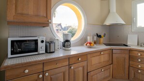 Une cuisine avec des meubles en bois, un four à micro-ondes, une machine à café et une fenêtre donnant sur des maisons.