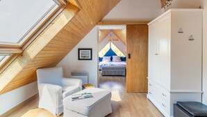 Un dormitorio acogedor en un ático con techo de madera inclinado, una cama con dosel azul y un armario blanco.