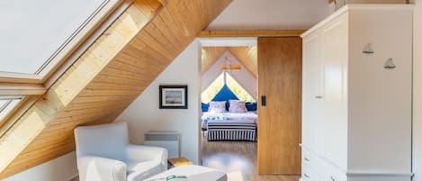 A cozy attic bedroom with a sloped wooden ceiling, a bed with a blue canopy, and a white wardrobe.