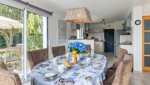 Un comedor con una mesa dispuesta para cuatro, una lámpara colgante de mimbre y vistas de la cocina y la zona de estar exterior.