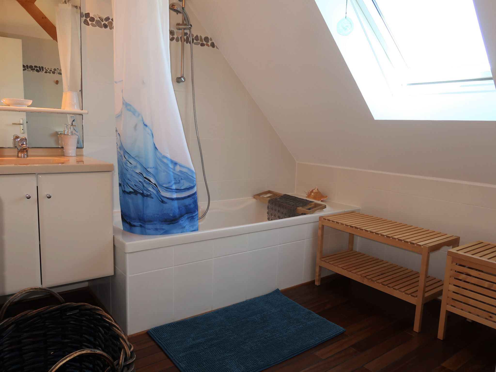 A bathroom with a bathtub, a wooden shelf, a blue rug, and a shower curtain with a wave design.