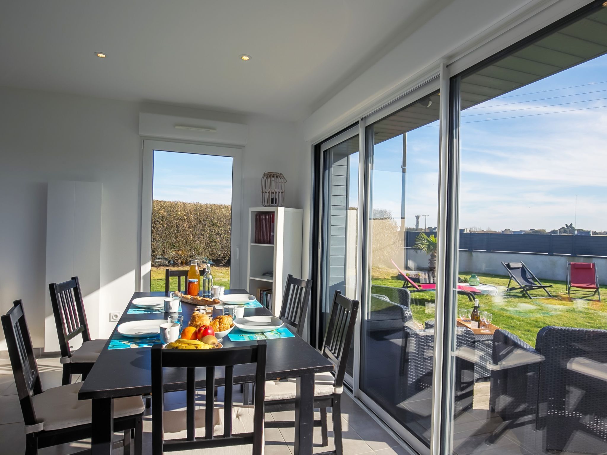 A dining area with a table set for four, a bookshelf, and a view of the backyard with outdoor furniture.