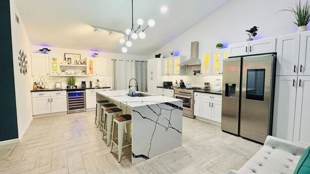 Cocina moderna con isla central, armarios blancos, electrodomésticos de acero inoxidable y un suelo con patrón de espiga.