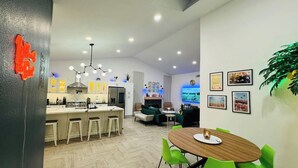 Una cocina moderna con una isla central, taburetes de bar y un área de comedor con una mesa redonda y sillas verdes.