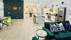 Una cocina moderna con armarios blancos, una isla central y una zona de comedor con una mesa redonda y sillas.