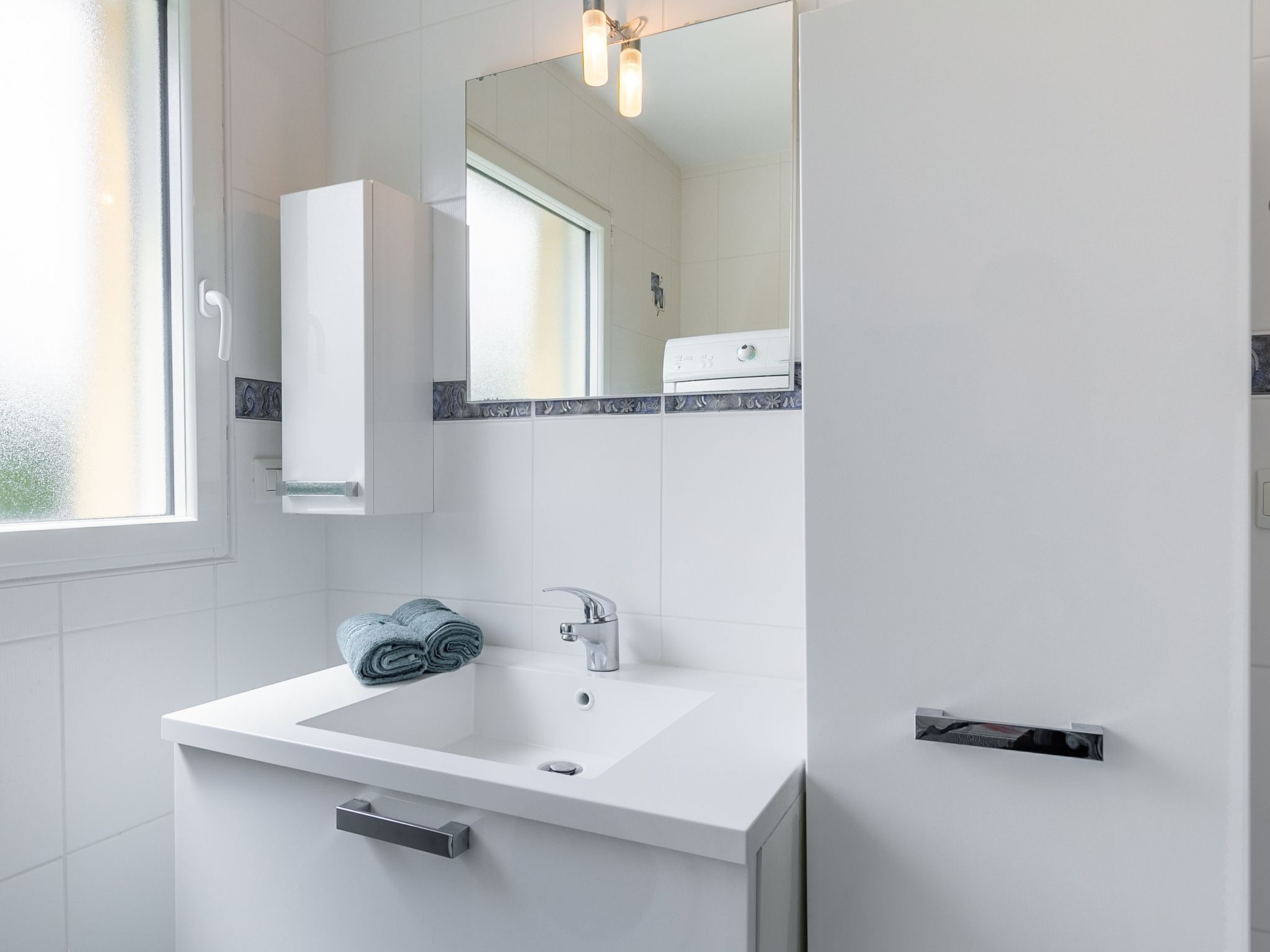 Een moderne badkamer met een witte wastafel, een spiegel en een handdoekhouder.
