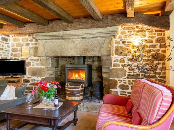 A cozy living room with a stone fireplace, a television, a sofa, and a coffee table with wine glasses and flowers.