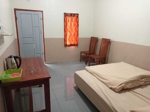 A room with a bed, a wooden table with a kettle and a glass, two wooden chairs, and a window with orange curtains. - Tengger Indah Seruni Bromo (Ngadisari)