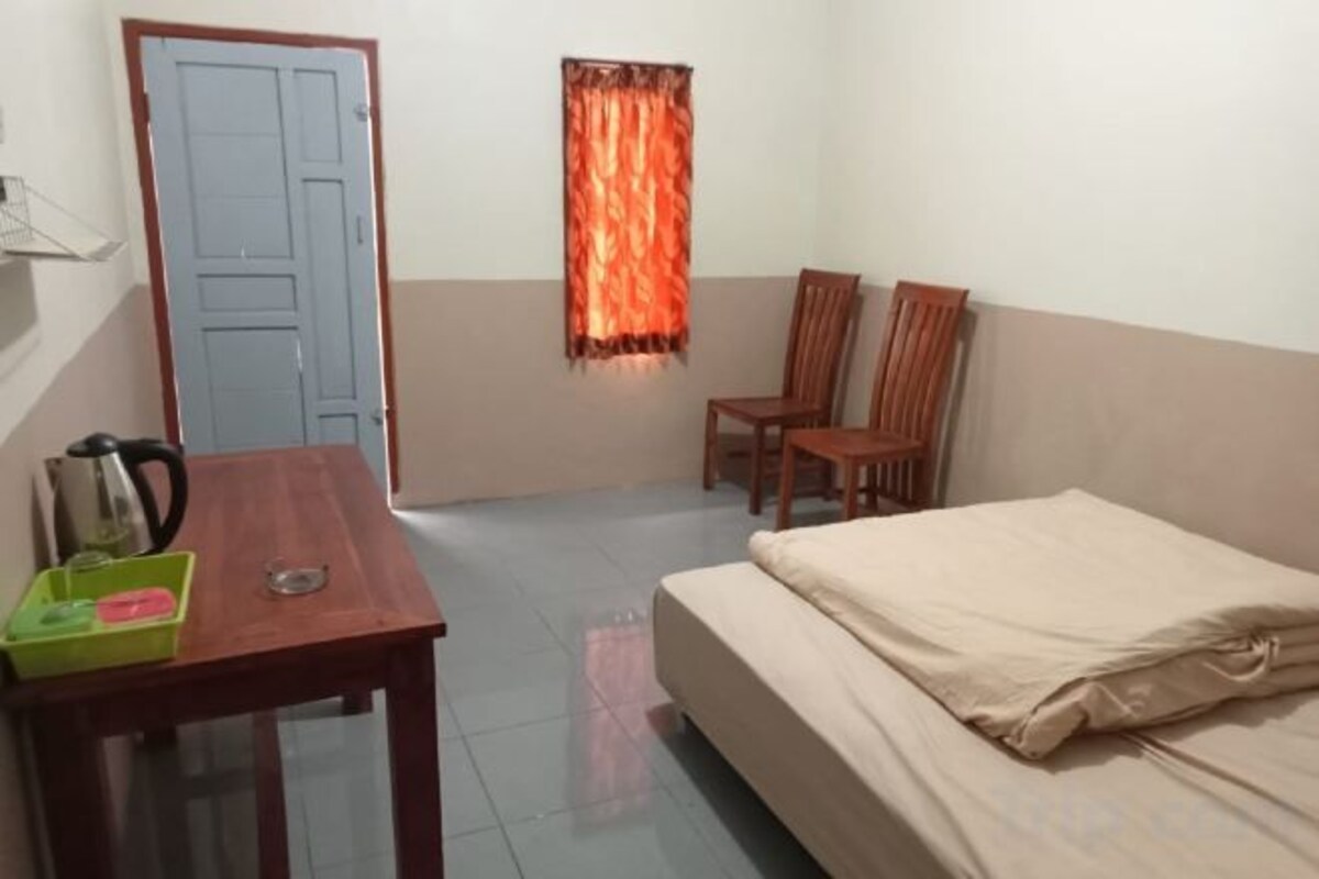 A room with a bed, a table with a kettle, chairs, and a door.