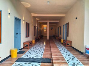 A hotel corridor with wooden benches, patterned floor tiles, and doors on both sides. - Tengger Indah Seruni Bromo (Ngadisari)