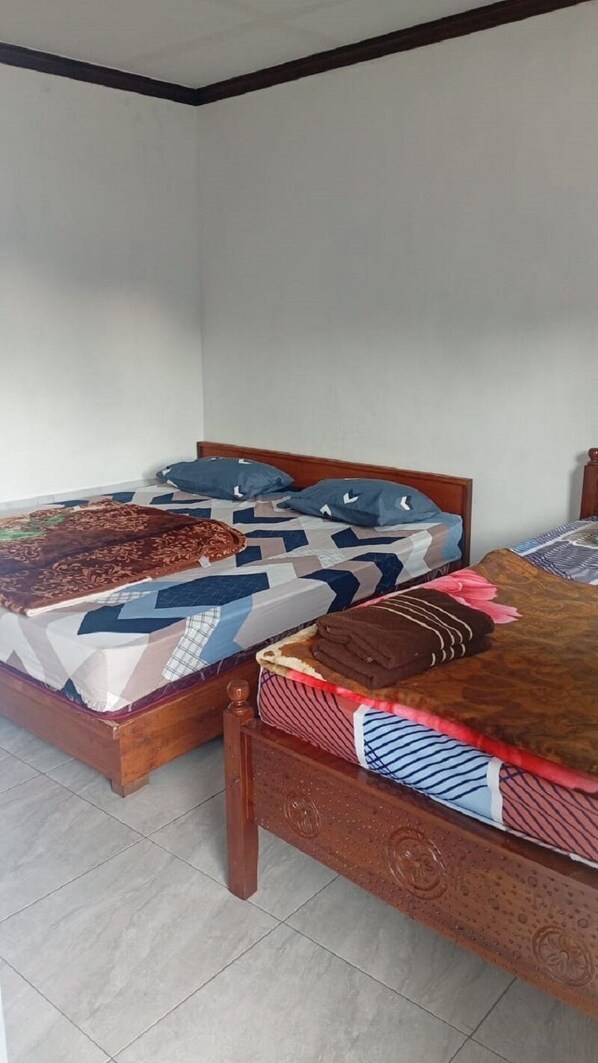Dos camas de madera con ropa de cama estampada en una habitación con paredes lisas y suelo de baldosas.