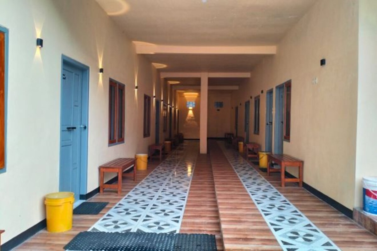 A long hallway with wooden benches and yellow trash bins, leading to a central area with a light fixture.