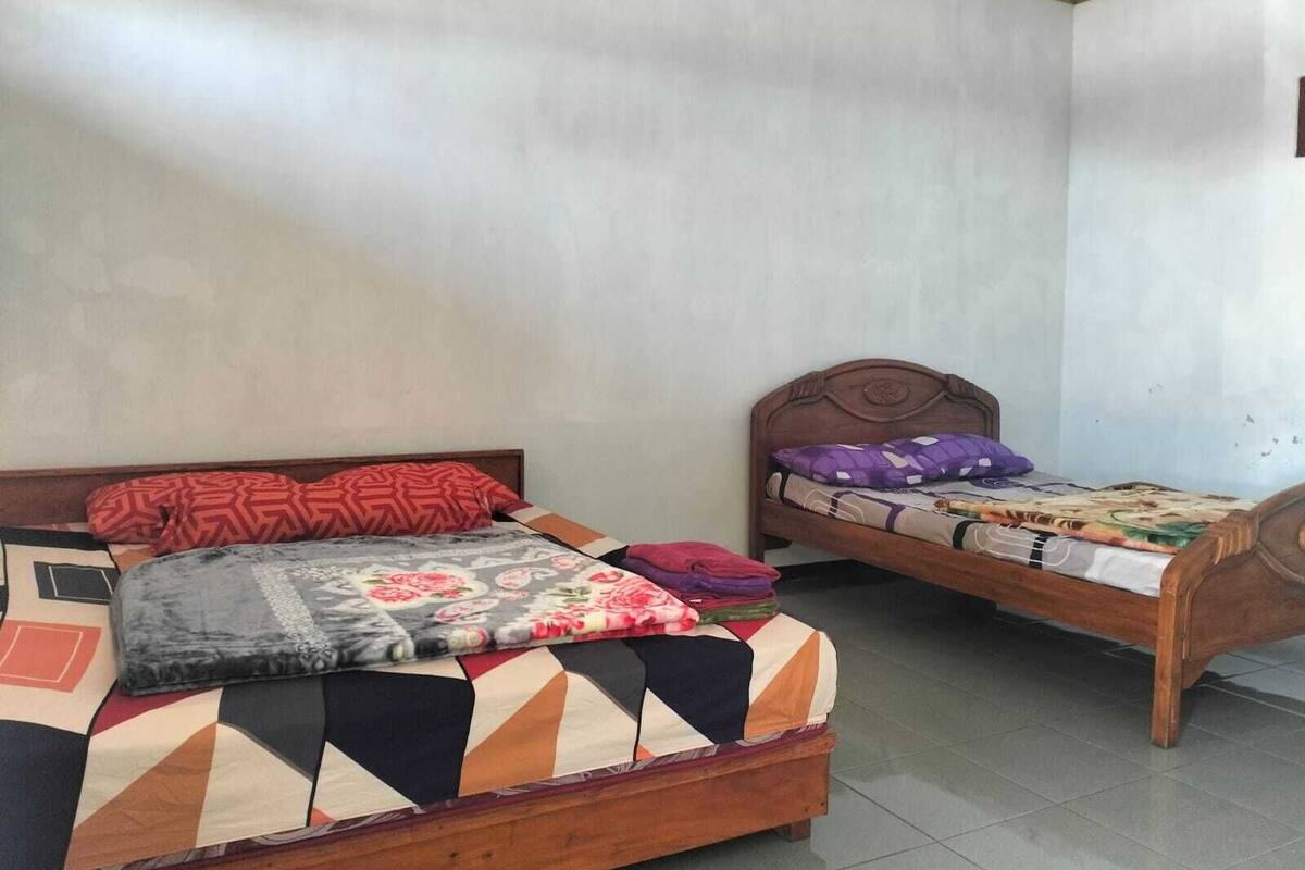 A room with two wooden beds, one with a floral bedspread and the other with a geometric pattern.