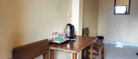 A room with a wooden table, chairs, a kettle, and a tray with bottles and glasses.