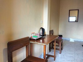 A room with a wooden table, chairs, a kettle, and a tray with bottles and glasses.