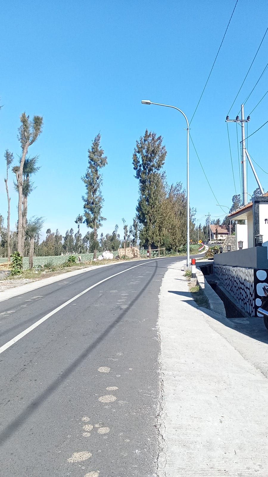 A road with a sidewalk, streetlights, and utility poles.