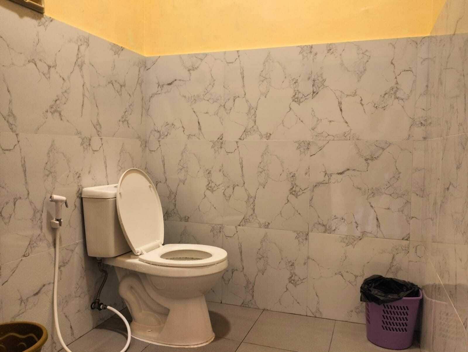 Ein Badezimmer mit Toilette, Wänden im Marmoroptik, einem Mülleimer und einer Duschkabine.
