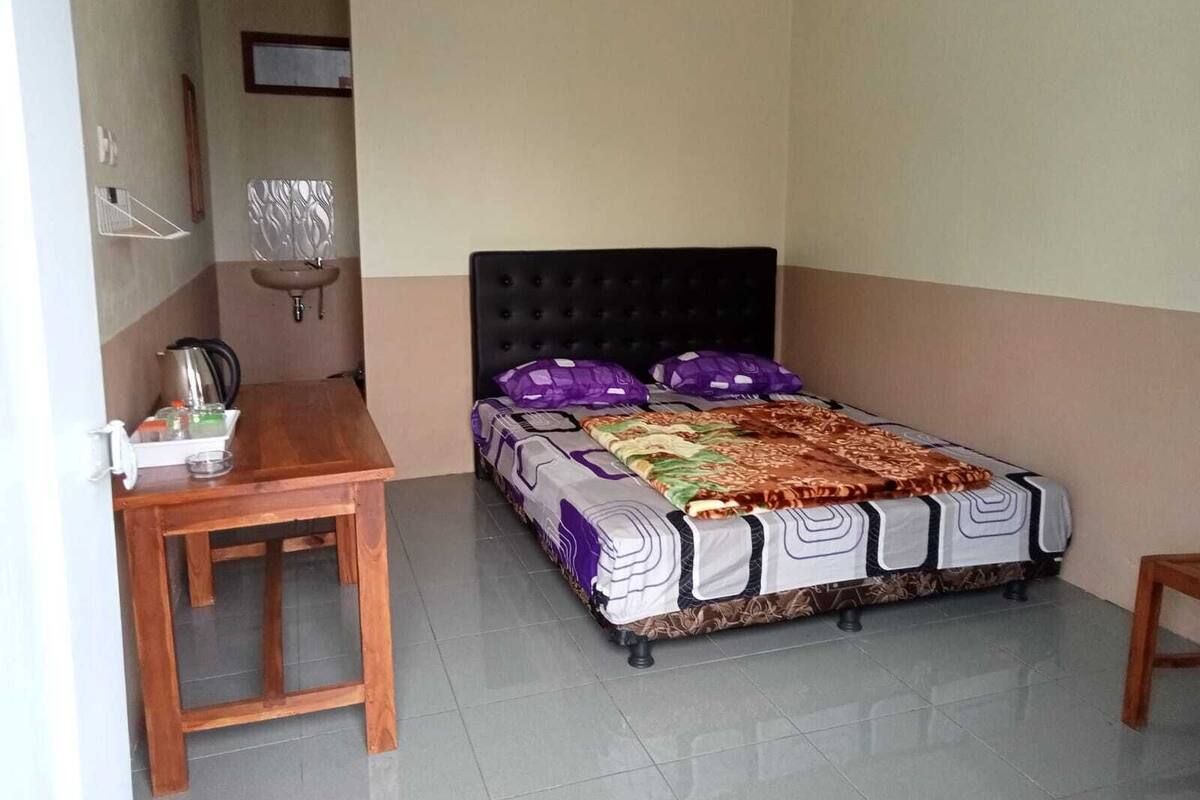Um quarto pequeno e bem arrumado, com uma cama, uma mesa de madeira e uma escrivaninha.