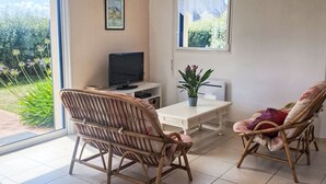 Una habitación con dos sillones de mimbre, una mesita, un televisor y una ventana con vistas a follaje.